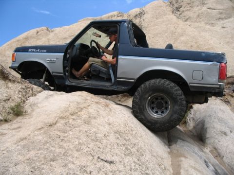 1989 Ford Bronco - A Ford Bronco navigates a rocky terrain with its doors open, its off-road capabilities.