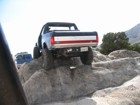 1989 Ford Bronco - A modified Ford Bronco navigates a rocky terrain, with another blue vehicle visible in the background.