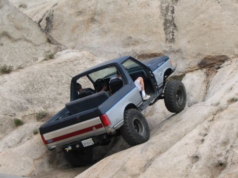 1989 Ford Bronco - This modified truck navigates a steep, rocky terrain with its doors open.