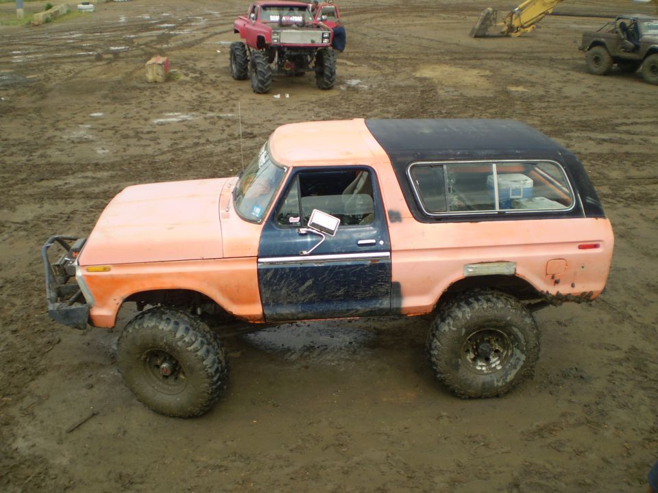 Orange and dark blue 1978 Ford Bronco with large tires, lifted suspension, and a black roof, parked in mud