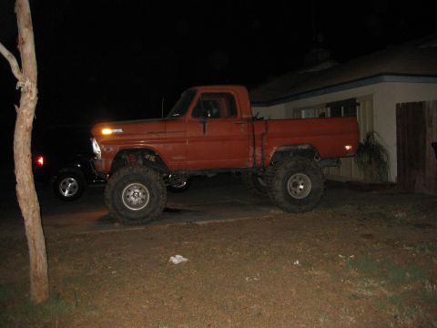 1969 Ford F-250 - Orange Ford F-series pickup truck with large tires parked outside a house at night.
