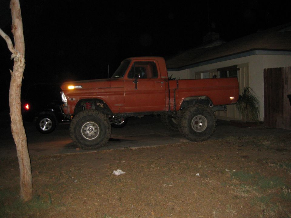 Lifted orange 1967 Ford F-series pickup truck parked next to a black SUV at night