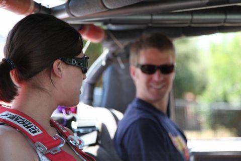 1989 Ford Bronco - A woman wearing a racing harness and sunglasses looks away from the camera while a man in sunglasses smiles in the background inside a vehi…