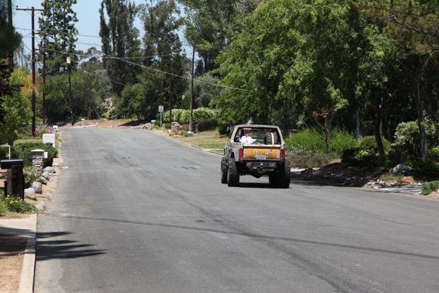 Tan topless SUV with roll bar driving away down a tree-lined street leaving tire marks