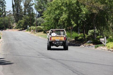 1989 Ford Bronco - A lifted Ford Bronco with a yellow tailgate drives down a residential road.