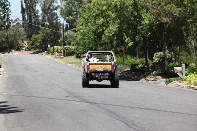 Lifted topless truck with roll bar driving away down a tree-lined street on oversized tires