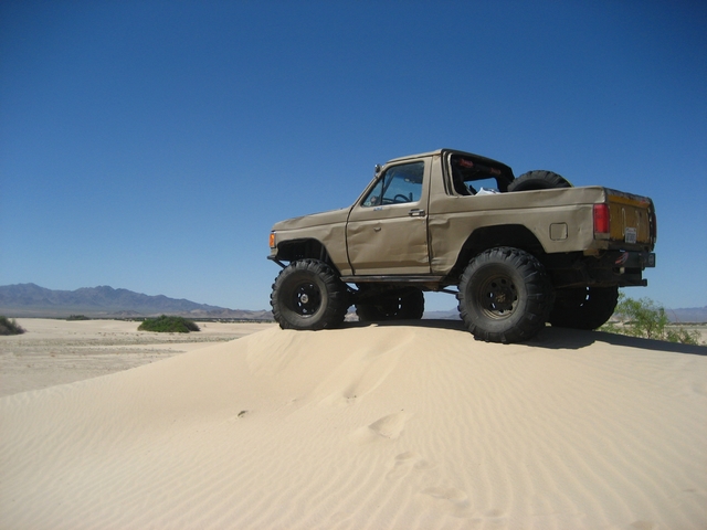 Tan topless lifted Ford Bronco parked on a desert sand dune under blue sky