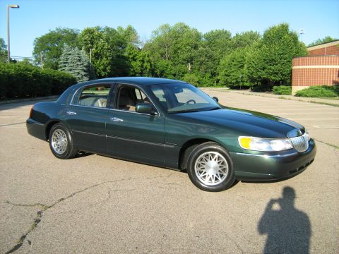 1988 Mercury Grand Marquis - This green 2001 Lincoln Town Car is parked on an asphalt lot with trees in the background.