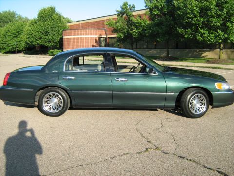 1988 Mercury Grand Marquis - A green sedan is shown from the side, parked on a cracked asphalt surface with a building and trees behind it.
