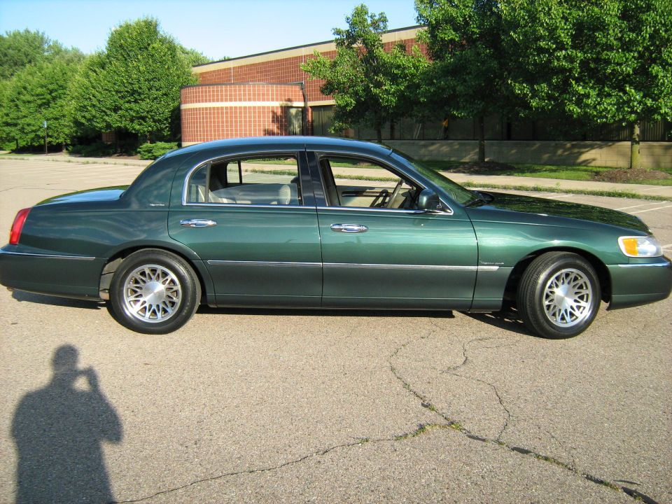 Green sedan parked on asphalt, side view. Building and trees in background