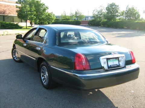 1988 Mercury Grand Marquis - The rear of a dark green Lincoln Town Car is shown parked on an asphalt surface with trees and a building in the background.