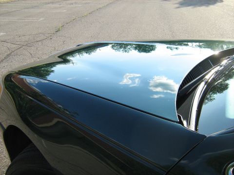 1988 Mercury Grand Marquis - Detail of a dark green car's hood and fender, reflecting the sky and trees. The Supermotors logo is visible in the lower right corner.