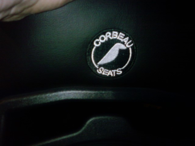 Close-up of a Corbeau Seats logo patch on black upholstery