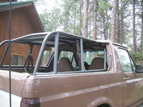1993 Ford Bronco - Side view of a topless brown two-tone Ford Bronco with its hardtop removed, revealing a full welded internal roll cage with hoops, door bar…