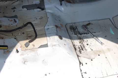 1994 Ford Bronco - Stripped-out cab floor of a truck with the carpet, seats and console removed, showing bare white-painted sheet metal with peeling factory s…