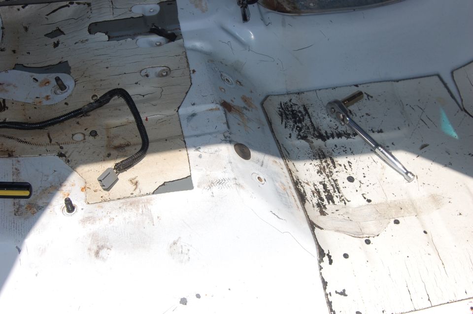 Bare stripped truck cab floor with peeling sealer, rust spots and a ratchet lying on it