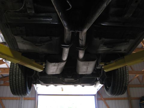 1985 Ford Mustang - The underside of a vehicle is visible, supported by yellow lift arms, with a dual exhaust system.