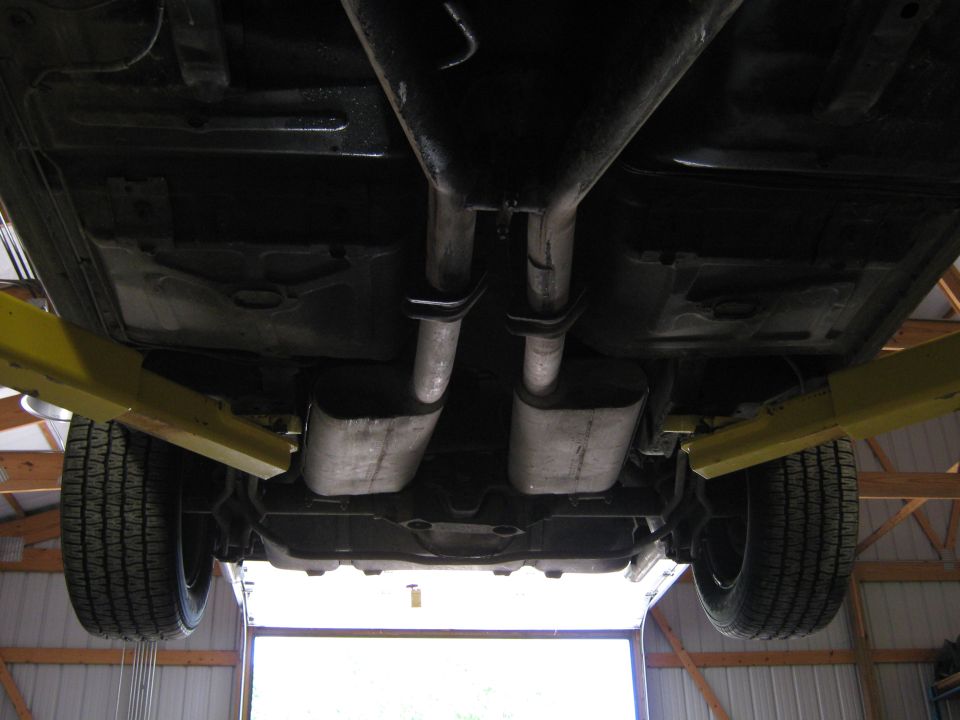 Undercarriage of a car on a lift, showing dual exhaust pipes, mufflers, and tires