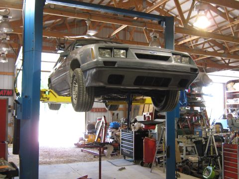 1985 Ford Mustang - A gray 1985 Ford Mustang is shown on a lift in a workshop, undergoing service.