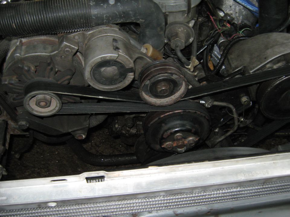 Engine bay with belts, pulleys, and hoses visible. Some dirt and grime present