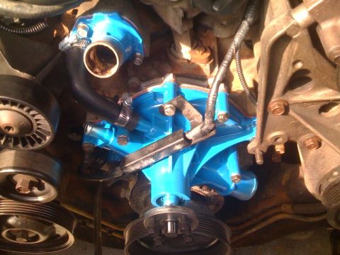 1996 Ford Bronco - Close-up view of a newly painted blue engine water pump assembly, showing hoses and drive pulleys.