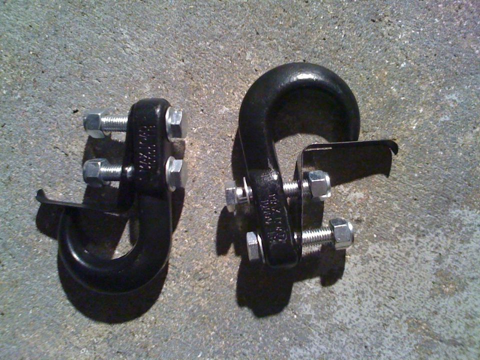 Two black tow hooks with bolts attached, resting on a concrete surface