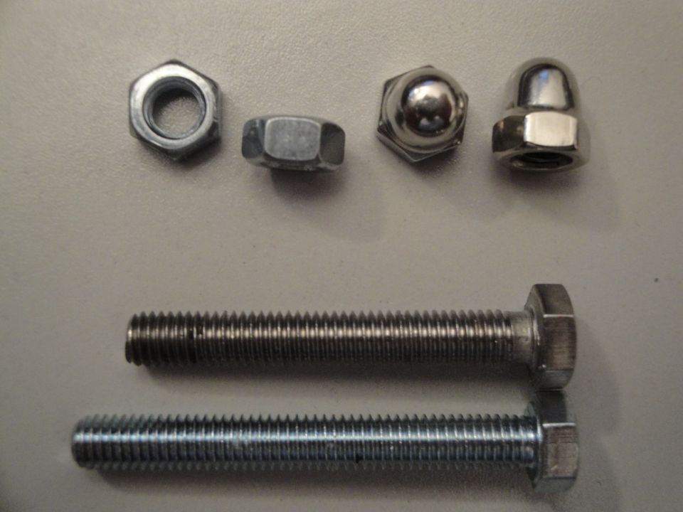 Two hex bolts and four nuts, two of which are acorn nuts, laid out on a flat surface