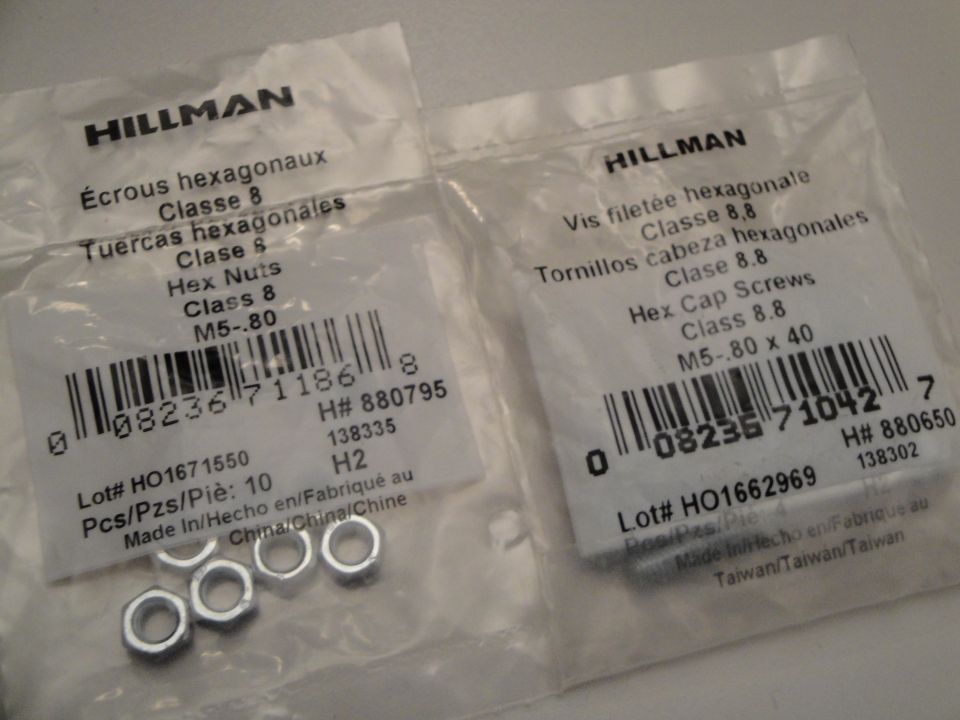 Two plastic packages of Hillman hardware, one with hex nuts and the other with hex cap screws, with visible barcodes and product information