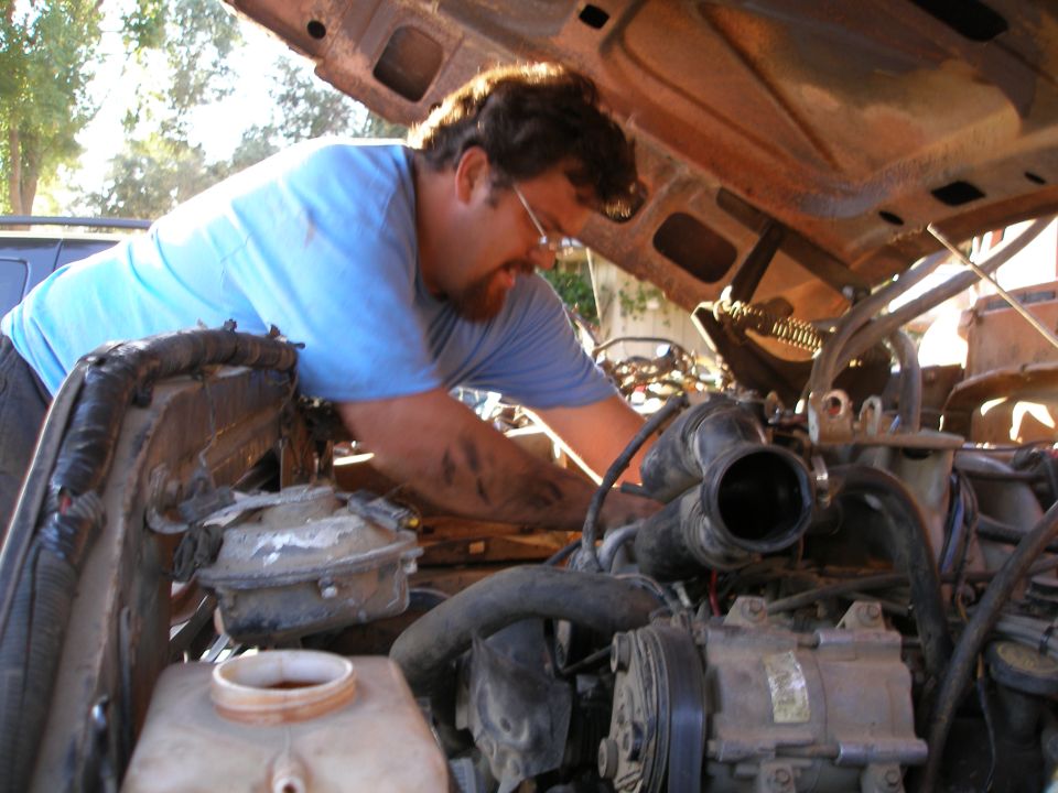 Man working on engine bay of a truck, hood open. Some engine parts visible