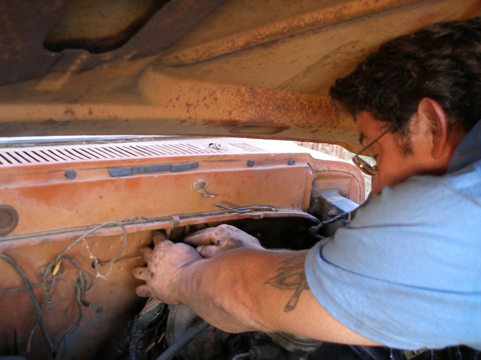 Man with glasses working on the engine bay of an old orange truck