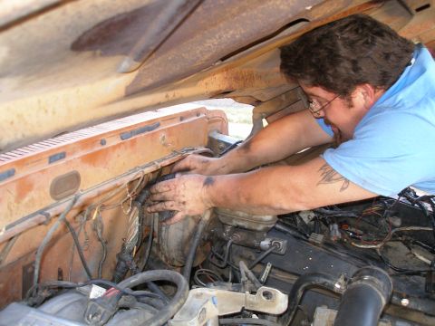 1969 Ford F-250 - A mechanic works on the engine bay of a vehicle, with visible rust and numerous wires.