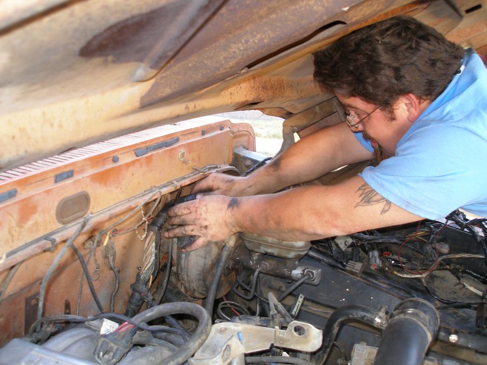 Man in blue shirt working on rusty orange engine bay, wires visible