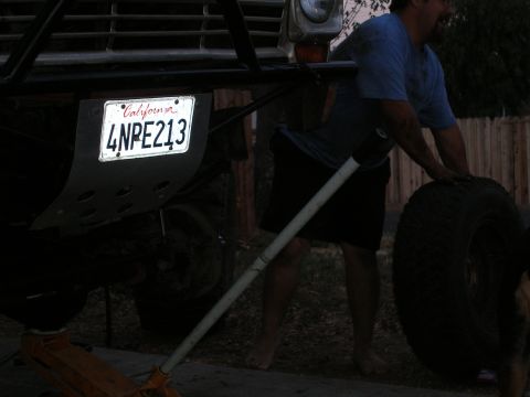 1969 Ford F-250 - A man changes a tire on a 1969 Ford F-250, which is jacked up and shows its front end with a California license plate.