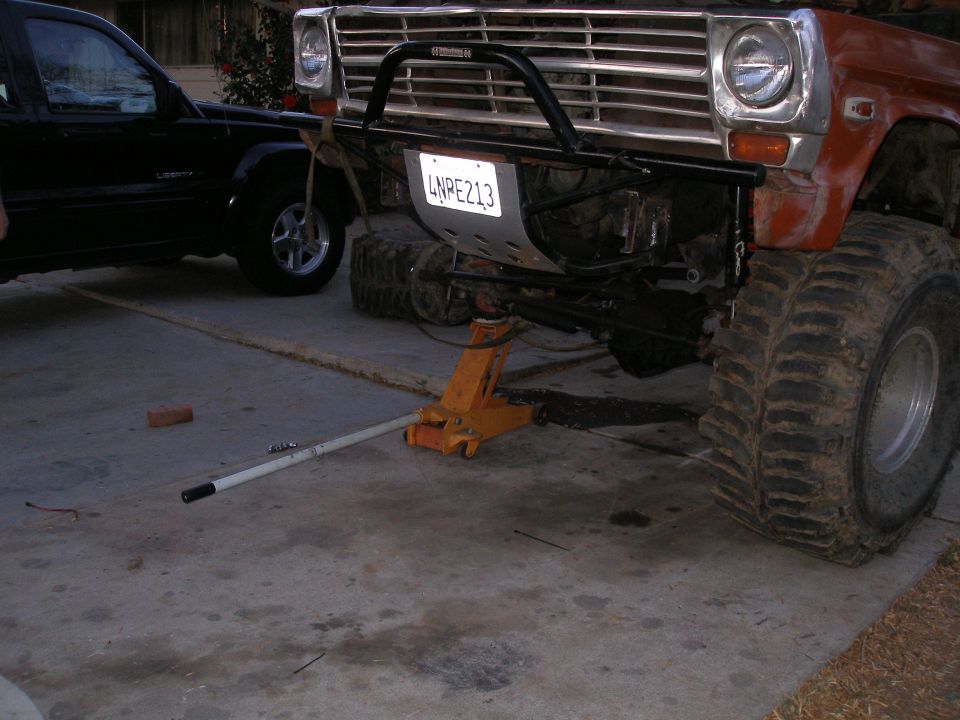 Orange off-road truck on jack, another black SUV parked nearby. License plate LNPE213