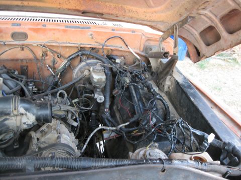 1969 Ford F-250 - The engine bay of an orange truck shows a complex network of wires and hoses, with a blue object visible behind the engine.