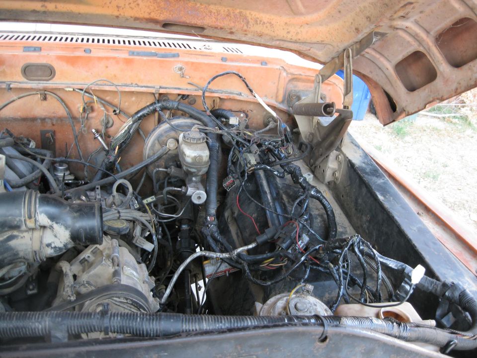 Orange truck engine bay with tangled wires and hoses. A blue object is visible in the background
