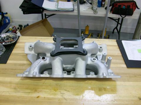 1973 Ford Ranchero - An aluminum intake manifold is shown on a wooden surface, with a gasket and bolts attached to the top.