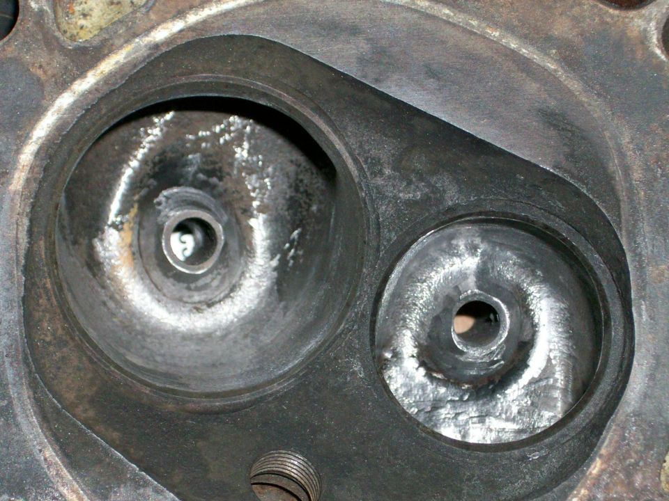 Close-up of an engine cylinder head with two combustion chambers visible. Watermark says SUPERMOTORS.NET