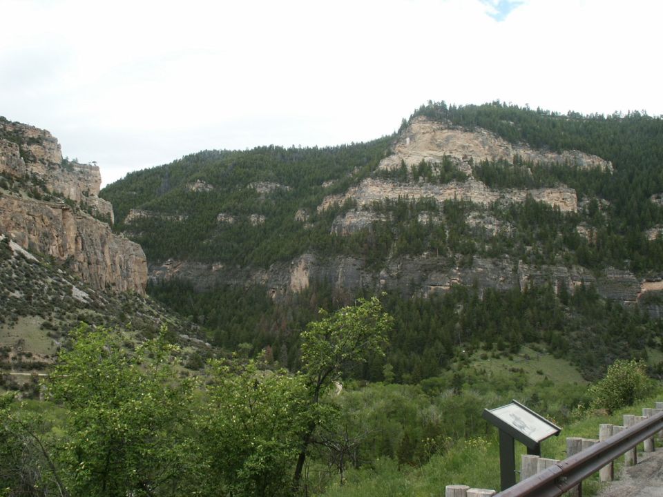 Mountain valley with trees and rock cliffs, a signpost is visible in the foreground