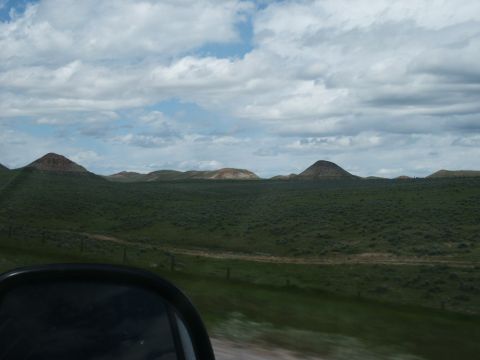 2000 Ford F-250 - A view from a vehicle's side mirror shows a wide expanse of green hills and a dirt road under a dramatic sky.