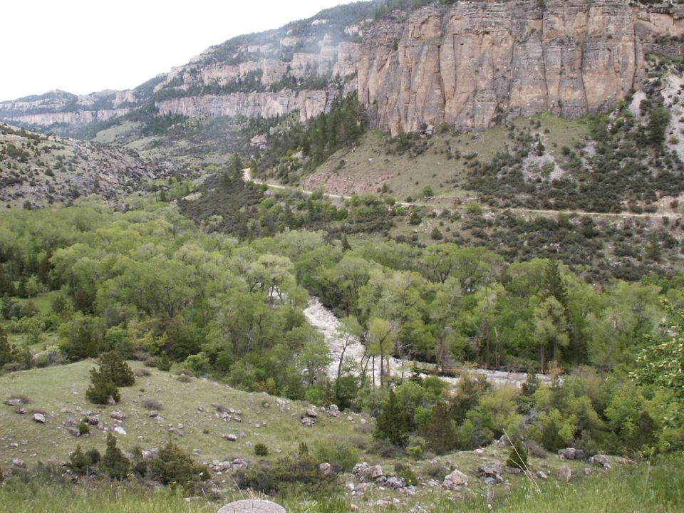 Mountain valley with a winding dirt road and a river, surrounded by trees and cliffs