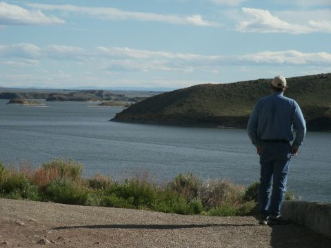 2000 Ford F-250 - A man stands on a ledge, gazing at a vast lake surrounded by rolling hills under a partly cloudy sky.