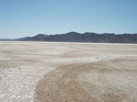 2000 Ford F-250 - A wide, arid landscape stretches out towards a mountain range, marked by the tracks of vehicles on the dry, cracked earth.