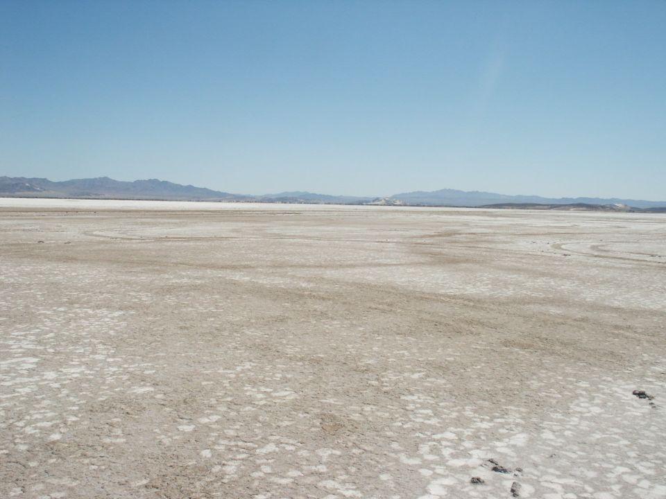 Vast dry lake bed under a clear blue sky with distant mountains