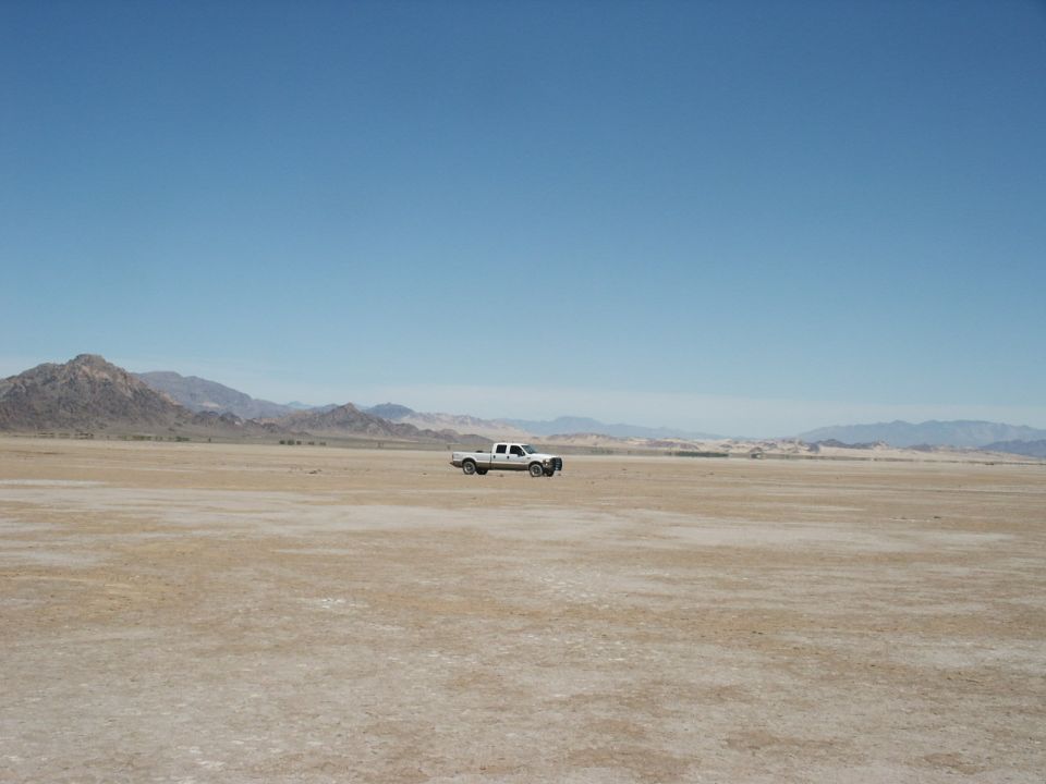 White 2000 Ford F-250 pickup truck parked in a dry, flat, desert landscape under a clear blue sky