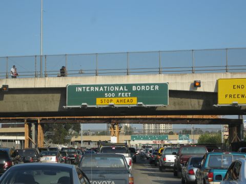 1986 Ford Bronco - Cars are backed up at a border crossing, with overhead signs indicating the proximity to the international border and the end of the freewa…