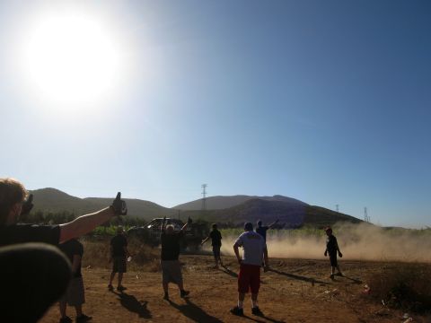 1986 Ford Bronco - Dust billows as off-road vehicles navigate a dirt track under a bright sun.