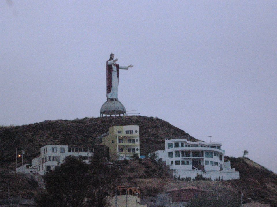 Christ the Redeemer statue overlooking buildings on a hill under a cloudy sky. Supermotors.net logo visible