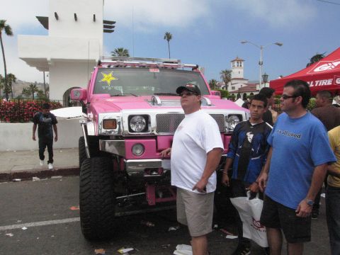 1986 Ford Bronco - A group of people stand near a bright pink Hummer H2 parked outdoors.