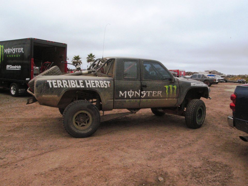 Side view of a dirt-covered off-road truck with "TERRIBLE HERBST" and "MONSTER" logos